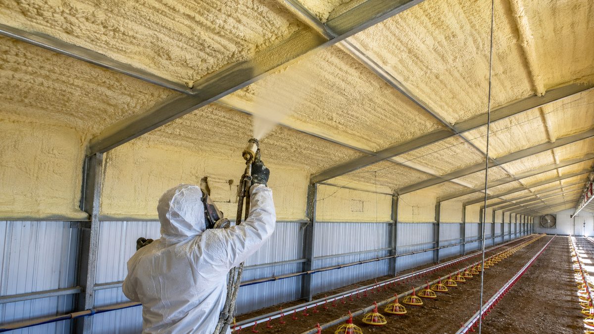 Operator spray-applying closed-cell polyurethane foam insulation inside a commercial poultry house